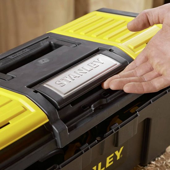 Hand op een zilveren Stanley-logo op de zwarte gereedschapskoffer met gele deksels.