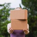 Deux blocs de yoga en liège marron empilés, tenus par une femme portant un haut violet.