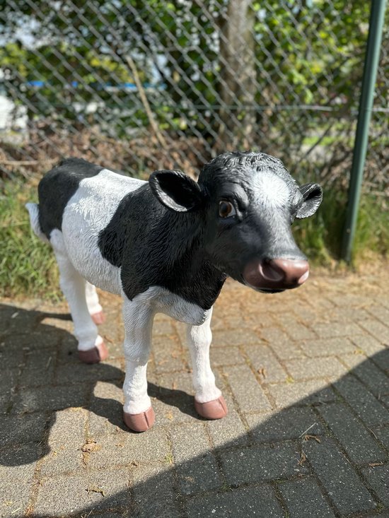 Un veau noir et blanc aux détails réalistes se tient sur une terrasse pavée.