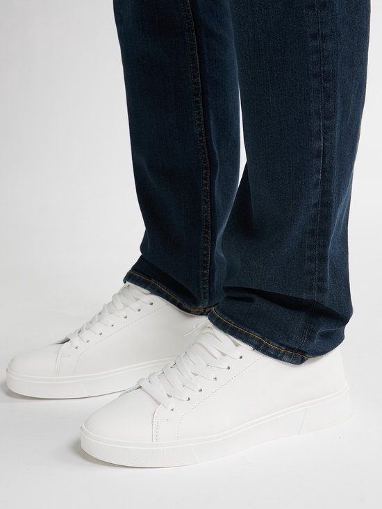 Onderlichaam van man in donkerblauwe jeans en witte sneakers.