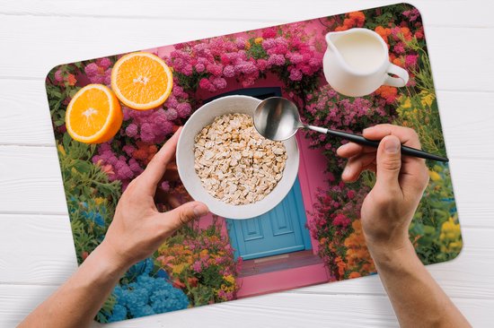 Set de table avec un imprimé d'une maison rose avec une porte bleue, entourée de fleurs, avec des céréales, une orange et du lait.