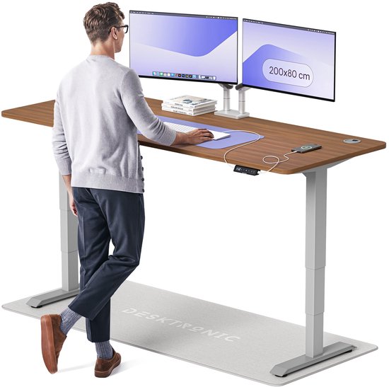 Man bij een groot bruin bureau met dubbele monitoren, staand op een grijs DESKTRONIC mat.