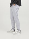 Man met lichtgrijze joggingbroek en witte sneakers, gedragen met een donkere jas.