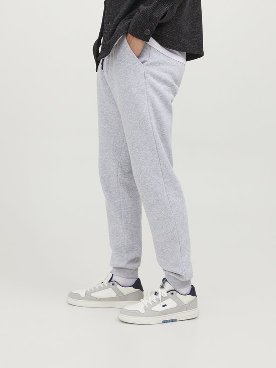 Man met lichtgrijze joggingbroek en witte sneakers, gedragen met een donkere jas.