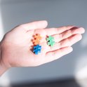 Hand die drie Plus-Plus bouwstenen vasthoudt: twee oranje, één blauwe en twee groene.