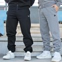 Drie kwart zicht op een zwarte en grijze joggingbroek met logo, gedragen door twee personen op een trap met sneakers.