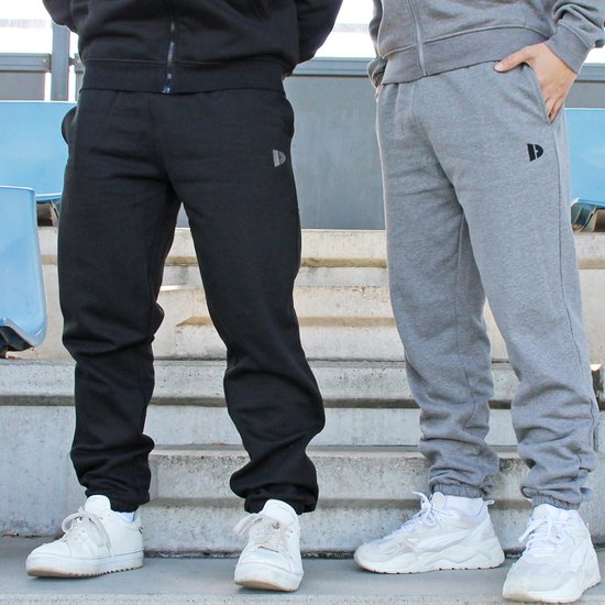 Drie kwart zicht op een zwarte en grijze joggingbroek met logo, gedragen door twee personen op een trap met sneakers.