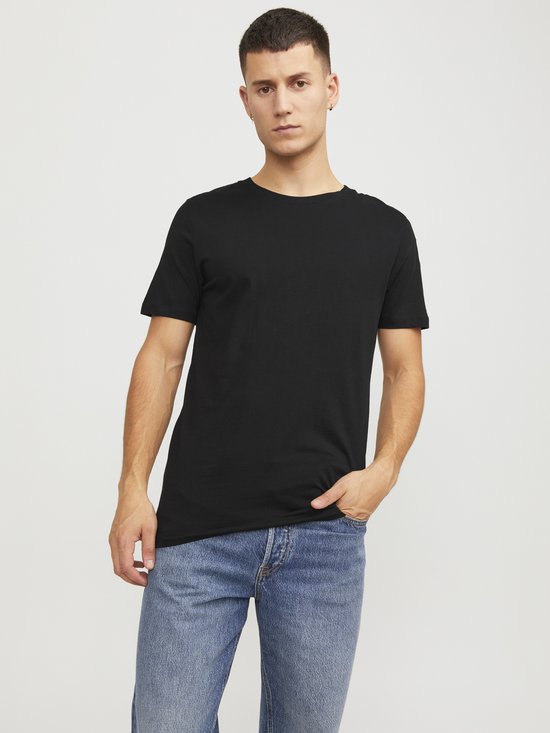Man met de hand in de zak draagt een zwart T-shirt en een spijkerbroek.