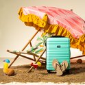 Groene koffer op het strand bij een ligstoel en parasol. Met slippers, drankjes en kokosnoten.