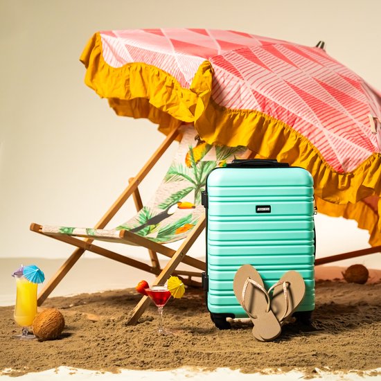 Groene koffer op het strand bij een ligstoel en parasol. Met slippers, drankjes en kokosnoten.