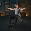 Man in grijs shirt traint met een zwarte fitnessbank en weerstandsbanden.