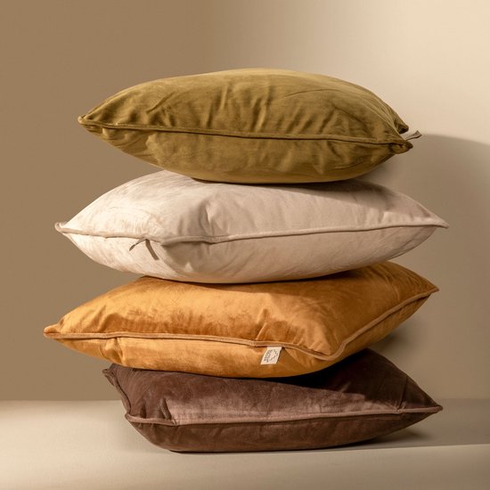 Een stapel van vier fluwelen kussens in de kleuren olijfgroen, lichtbeige, mosterdgeel en bruin, met het merklogo zichtbaar op het mosterdgele kussen.