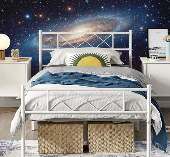Wit metalen bedframe met diamantpatroon hoofdbord en voetbord, achtergrond met melkwegstelsel en sterren.