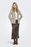 Model in een beige blazer, wit shirt en bruine leren rok. Staat met de handen achter de rug.