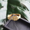 Gouden Casio dameshorloge met mesh band op een zwarte ondergrond, met groene plant op achtergrond.