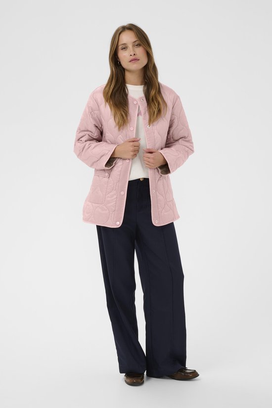 Model draagt een roze gewatteerde jas, open met witte top en donkerblauwe wijde broek.