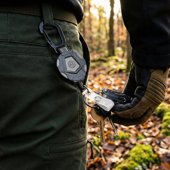 Porte-clés rétractable noir avec mousqueton, avec un trousseau de clés attaché, porté à la ceinture dans un environnement forestier.