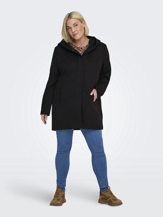 Vrouw met blonde haren, draagt een zwarte lange jas met capuchon, een top met dierenprint en spijkerbroek.