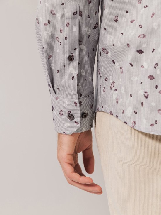 Detail van de mouw van een grijs overhemd met paarse en witte bloemenprint.