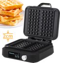 Open zwart wafelijzer met twee lege wafelvormige vakken en een stapel wafels ernaast.