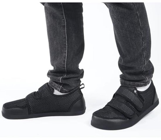 Een persoon die zwarte ademende mesh schoenen met klittenbandsluiting draagt.