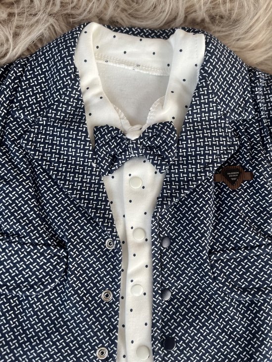 Donkerblauwe blazer met witte print en bijpassend wit poloshirt met stippen en strikje.