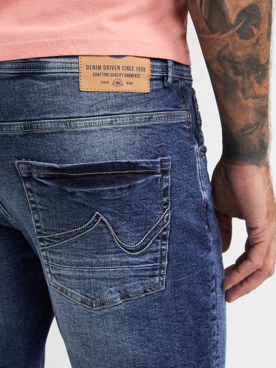 Detail van de achterzakken van een spijkerbroek met een bruin leren label met "DENIM DRIVEN SINCE 1989".