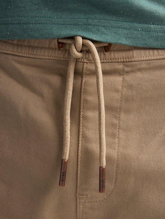 Sluiting van een beige chino short met beige veter en koperkleurige uiteinden met 'Petrol' opdruk.