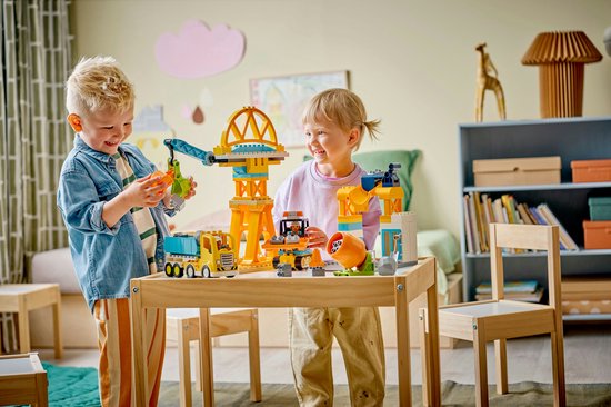 Twee lachende kinderen spelen met geel bouwspeelgoed met kranen en voertuigen.