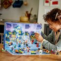 Meisje met krullend haar dat een LEGO Adventskalender opent. De kalender toont een besneeuwde stad met genummerde deurtjes.