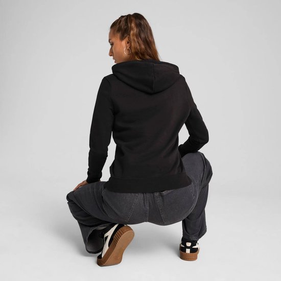 Vrouw zittend in een zwarte hoodie met grote jeans.