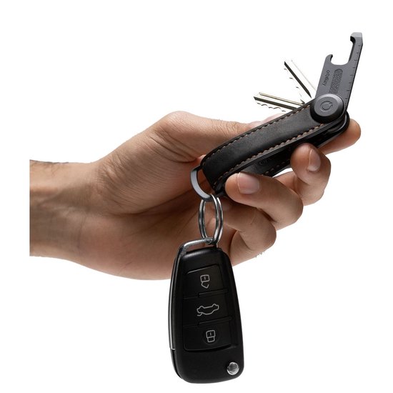Hand met zwarte Orbitkey lederen sleutelorganizer met sleutels en autosleutel.
