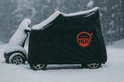 Zwarte scootmobielhoes met rode HOC-logo, bedekt met sneeuw.