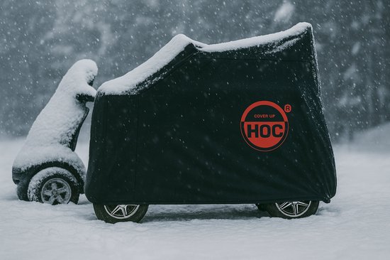 Zwarte scootmobielhoes met rode HOC-logo, bedekt met sneeuw.