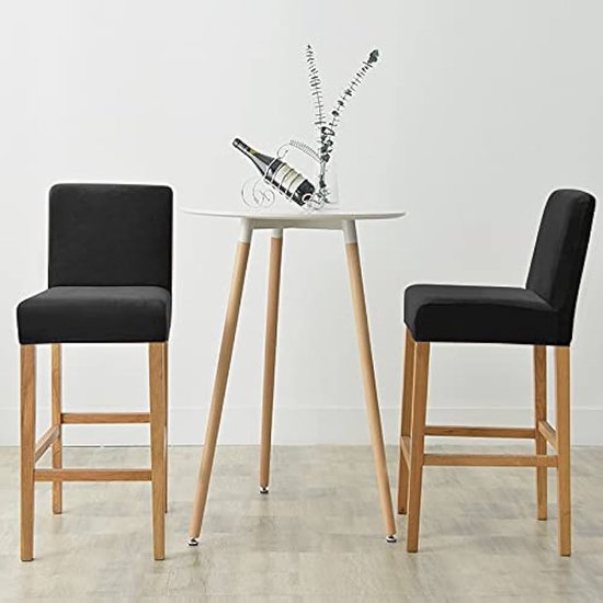 Twee zwarte fluwelen barkrukhoezen met houten poten, naast een ronde tafel.