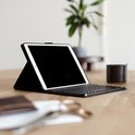 Zwarte tablet case met toetsenbord, staand op een houten tafel. Naast een plant en kopje.