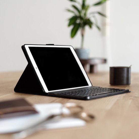 Zwarte tablet case met toetsenbord, staand op een houten tafel. Naast een plant en kopje.
