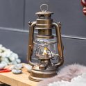 Bronzen Feuerhand stormlantaarn met vlam, staand op een houten plank.