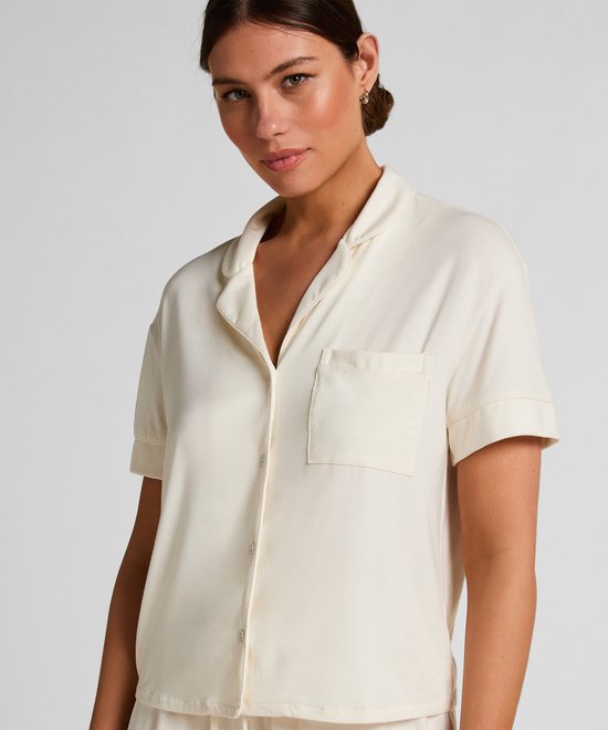 Model van voren, draagt een roomwit pyjamashirt met korte mouwen en een bijpassende pyjamashort. Zilveren oorbel.