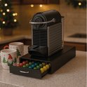 Boîte noire pour capsules, tiroir ouvert rempli de capsules colorées à côté d'une machine Nespresso et de tasses de Noël.