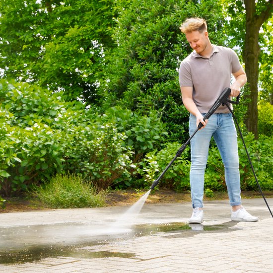 Man met hogedrukreiniger die een betegeld terras schoonspuit.