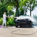 Vrouw spuit met hogedrukreiniger een zwarte auto schoon.