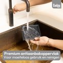 Een grijze grillplaat wordt schoongemaakt onder stromend water in een gootsteen.
