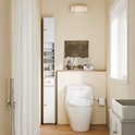 Witte smalle badkamerkast naast een toilet, met handdoeken en potjes op de planken.