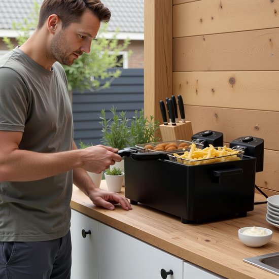 Man bereidt bitterballen en friet in een dubbele zwarte frituurpan buiten.