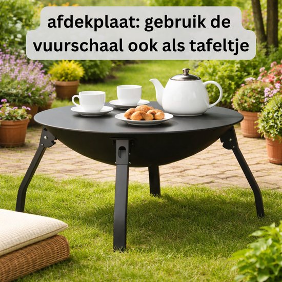 Zwarte vuurschaal in gebruik als tafel met kopjes, een schaal met koekjes en een theepot, in een tuinsetting.