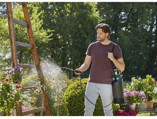 Man met donkergrijze GARDENA drukspuit met blauwe details op de schouder, sproeit planten.