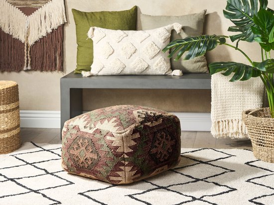 Een woonkamerinterieur met een poef met geometrisch patroon, kussens en een plant.