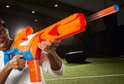 Man richt een oranje en blauwe Nerf N-Series Pinpoint blaster, die een oranje dart afvuurt.