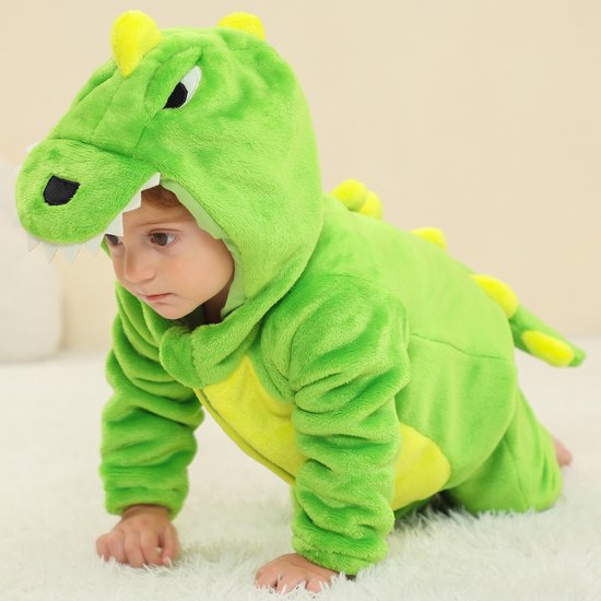 Baby in groene dinosaurus onesie, kruipend, met gele buik, kap met tanden en rugstekels.